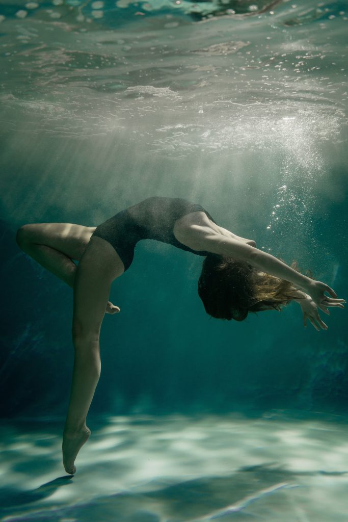 Elegant underwater photograph of a woman gracefully posing in a swimsuit, illuminated by natural light.