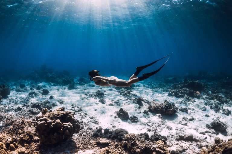 free-diver-woman-with-fins-glides-over-corals-in-blue-ocean voyage apnée polynésie